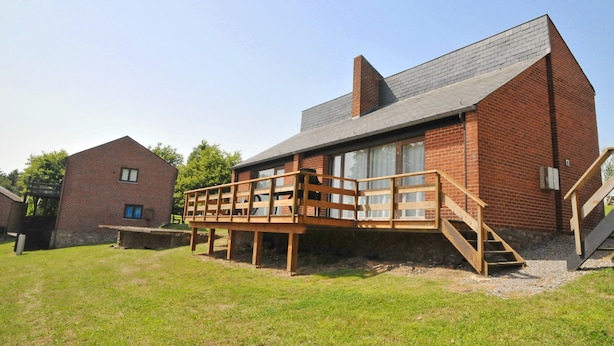 A modern brick building with a wooden deck and stairs leading to a glass door entrance. - Kangourou 2 (Hastiere)