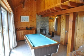 A wooden interior with a pool table, stone fireplace, wooden cabinets, and a stone wall.