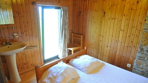A wooden cabin room with a bed, a window, a chair, and a sink. - Kangourou 2 (Hastiere)