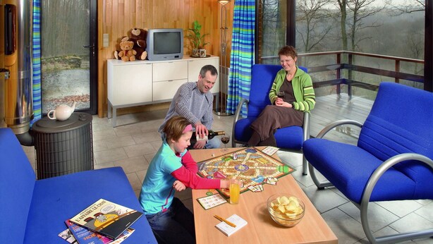 A cozy cabin interior with wooden walls, a large window, and a dining area with a board game. - Kangourou 6 (Hastiere)