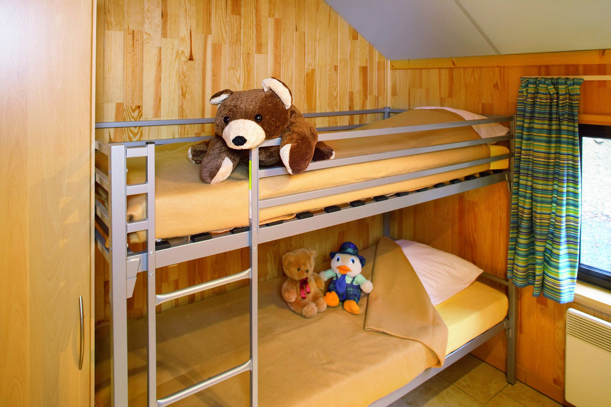 A bunk bed room with wooden walls, a window with curtains, and stuffed toys on the beds.