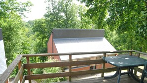 A wooden deck with a table and chairs, overlooking a brick building and lush greenery. - Kangourou 6 (Hastiere)