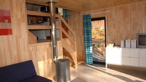 A wooden interior with a sofa, a table, a trash can, a staircase, and a view through a door. - Kangourou 6 (Hastiere)