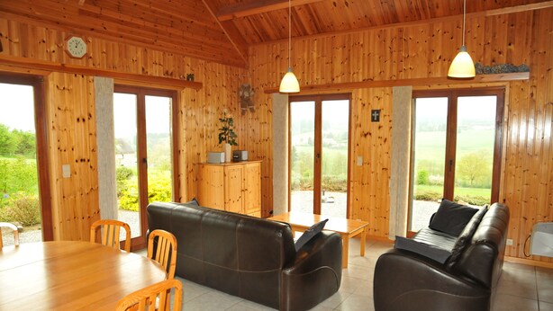 A wooden interior with a dining table, two leather sofas, and a small cabinet. - Laloux (Rochefort)