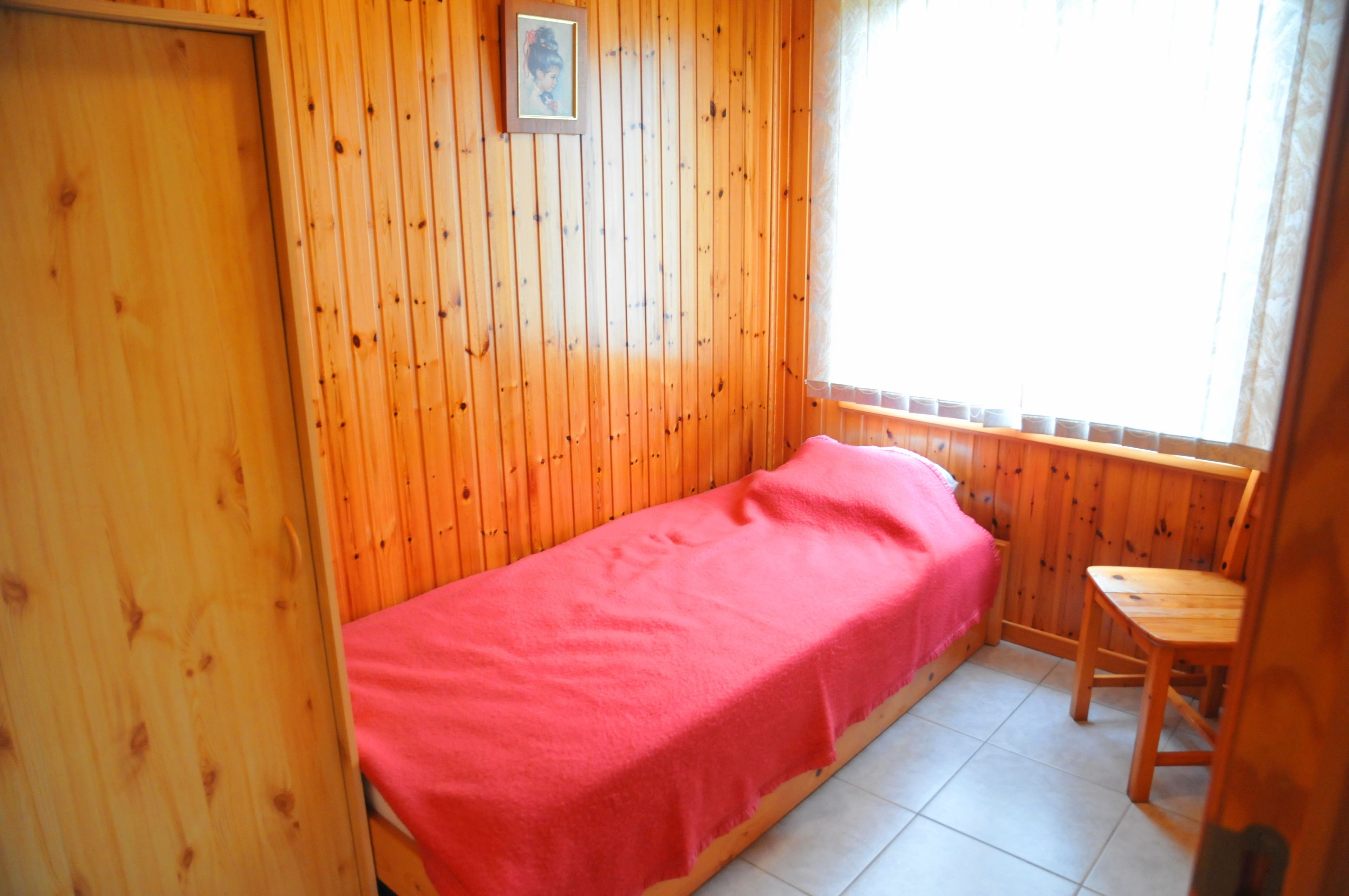 Ein kleines Zimmer mit einem Einzelbett, Holzwänden und einem Fenster.