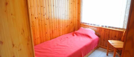 Ein kleines Zimmer mit einem Einzelbett, Holzwänden und einem Fenster.