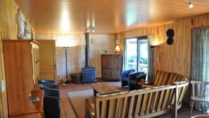 A cozy room with a wooden ceiling, a stone wall, a fireplace, a sofa, and a table. - Lindbergh (Durbuy)