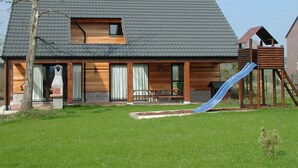 A two-story house with a sloped roof, a wooden deck, and a blue slide. - Lindbergh (Durbuy)