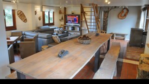 A spacious living area with a long wooden table, comfortable seating, a television, and a fireplace.