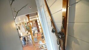 A narrow hallway with a wooden ladder, a white wall with a mounted bicycle, and a glimpse of a dining area with a table and chairs.