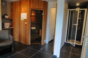 Una habitación con pared de paneles de madera, puerta de cristal que da a una zona de ducha y una silla.