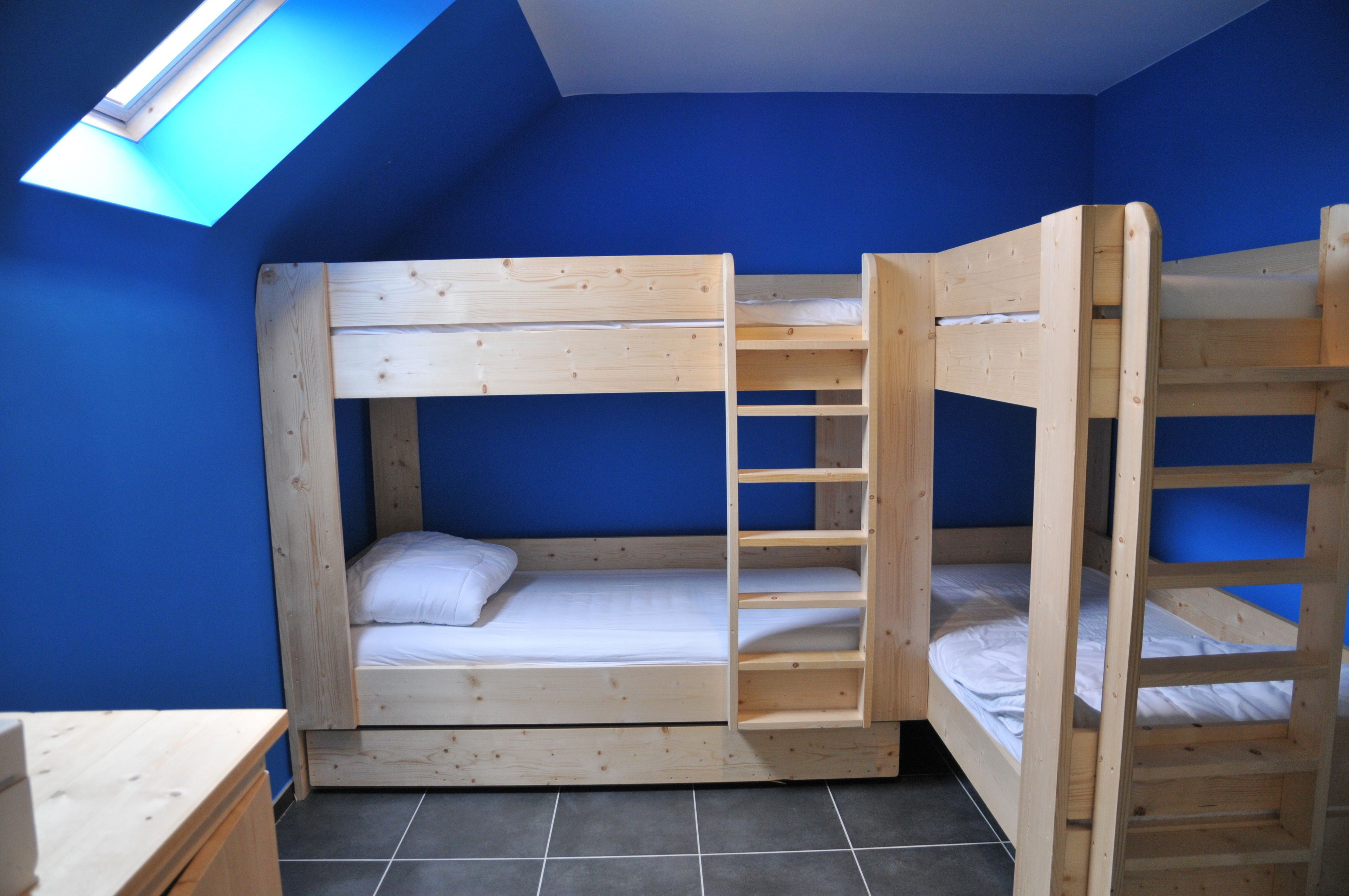 A room with two bunk beds, a skylight, and a small wooden desk.