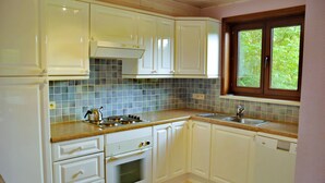 A kitchen with white cabinets, a tiled backsplash, a window, and a sink. - Petite Enneille (Durbuy)