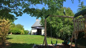 A backyard with a swing set, a playhouse, and a house in the background. - Petite Enneille (Durbuy)