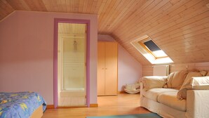 A bedroom with a sloped ceiling, wooden flooring, a bed with a blue floral bedspread, a beige sofa, and a skylight. - Petite Enneille (Durbuy)