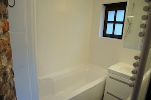 A bathroom with a bathtub, a small window, and a mirror with lights.