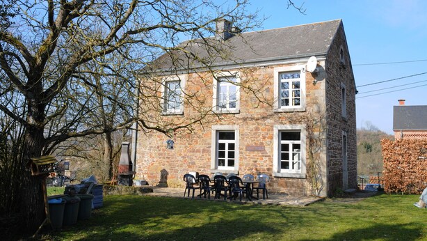 Un bâtiment en pierre doté d’une cheminée, d’une antenne parabolique et d’un petit jardin avec une table et des chaises.