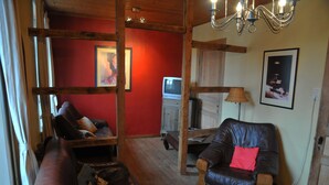 Un salon chaleureux avec un plafond en bois, un canapé en cuir, un fauteuil en bois et un téléviseur.