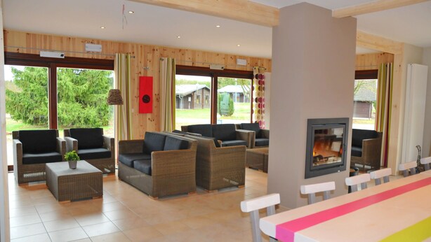 Een ruime woonkamer met rieten meubels, een open haard en grote ramen met uitzicht op de omgeving.