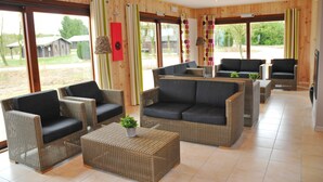 Een ruime kamer met rieten meubilair, grote ramen en uitzicht op de omgeving.