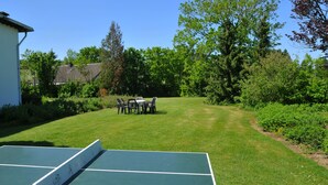 A tennis court with a net, surrounded by a grassy area with trees and a building in the background. - Résidence Thier Antoine (Somme-Leuze)