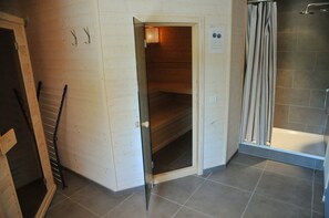 A wooden interior with a sauna, a shower area, and a door leading to a dark room.