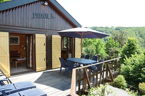 A wooden cabin with a deck, a table with chairs, and an umbrella. - Rochettes - Pluton 3 (La Roche-en-Ardenne)