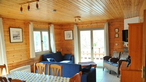 A wooden cabin interior with a dining table, blue sofa, and wicker chairs. - Rochettes - Vénus 1 (La Roche-en-Ardenne)