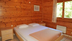 A wooden-paneled room with a bed, nightstands, a window, and a radiator. - Rochettes - Vénus 2 (La Roche-en-Ardenne)