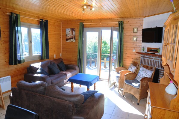 A cozy cabin interior with a brown leather sofa, wicker chairs, a blue table, and a fireplace. - Rochettes - Vénus 5 (La Roche-en-Ardenne)