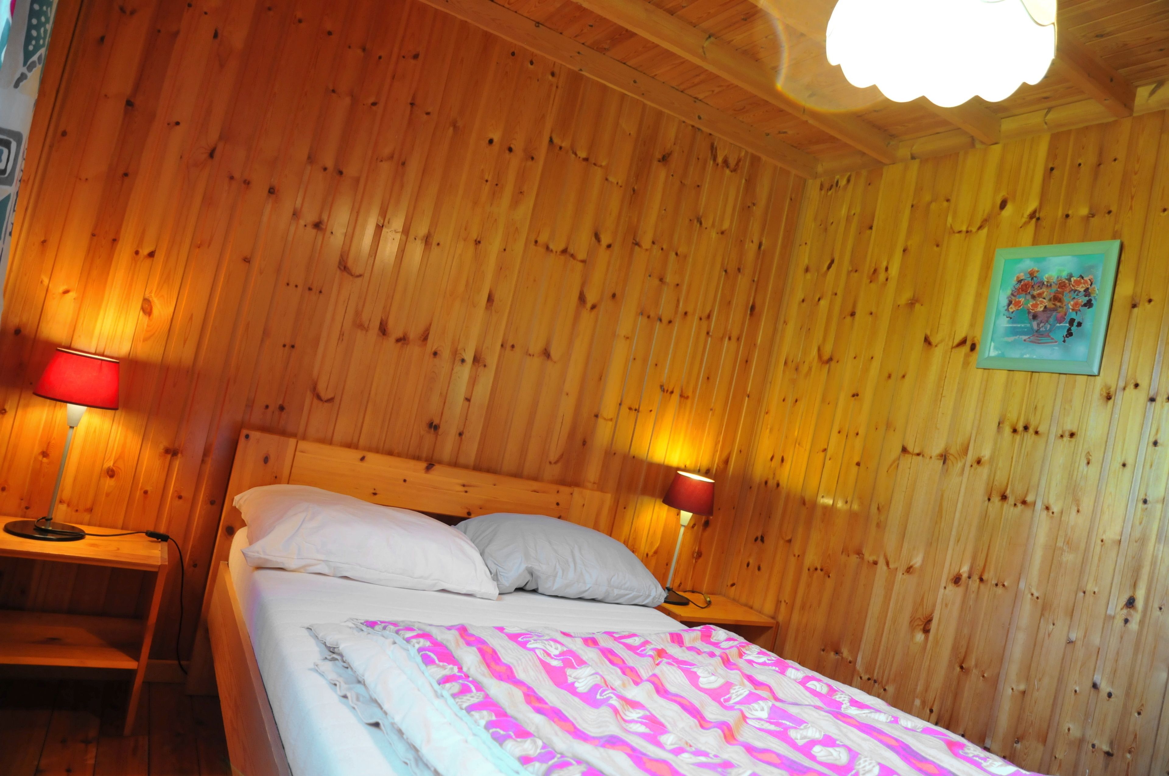 A wooden-paneled room with a bed, two bedside lamps, and a painting on the wall.
