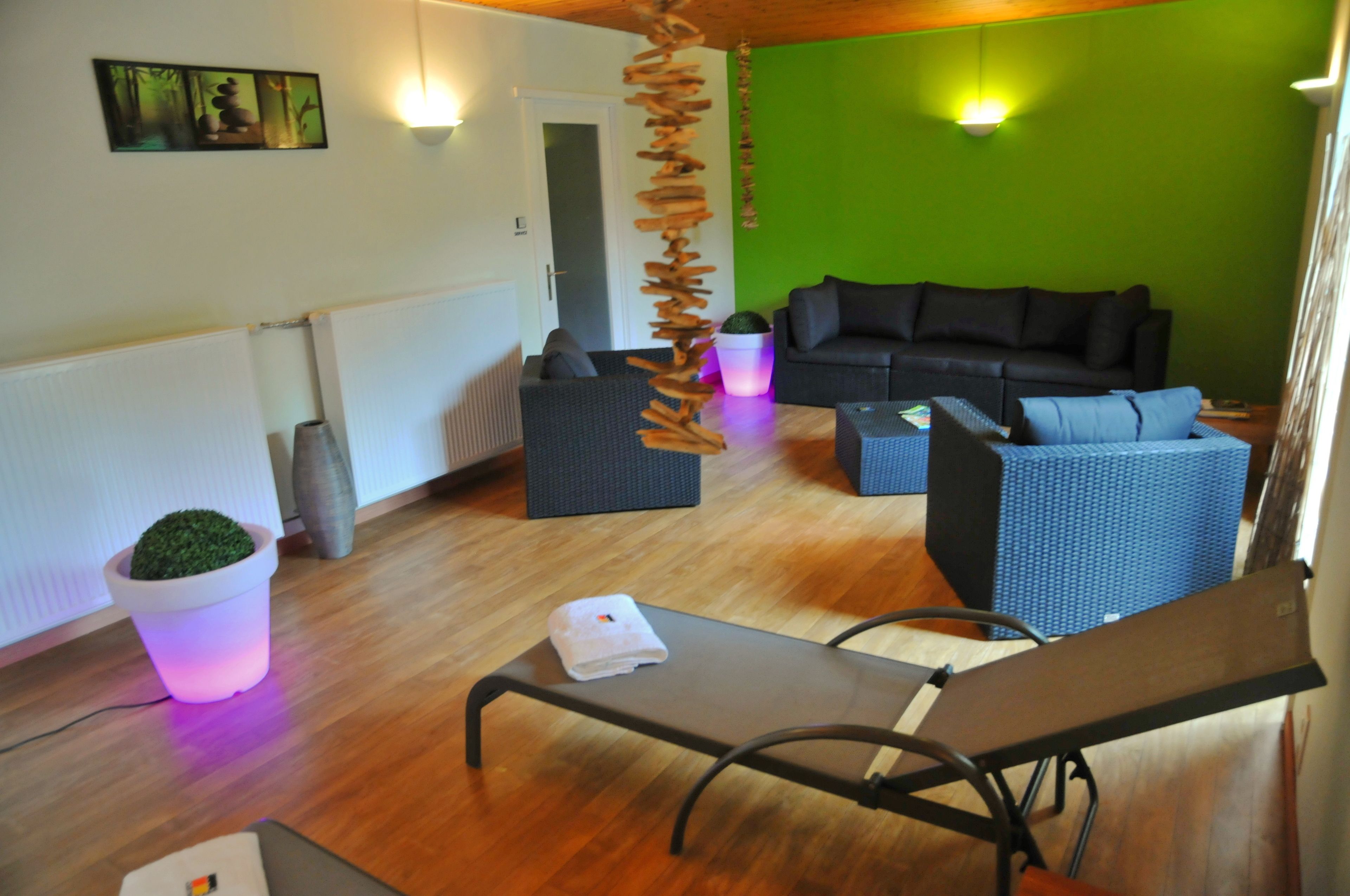 A room with a wooden floor, a black sofa, a blue chair, a small table with a towel, and a hanging decoration.