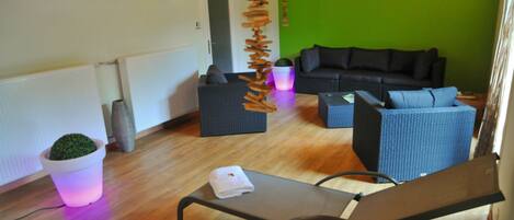 A room with a wooden floor, a black sofa, a blue chair, a small table with a towel, and a hanging decoration.