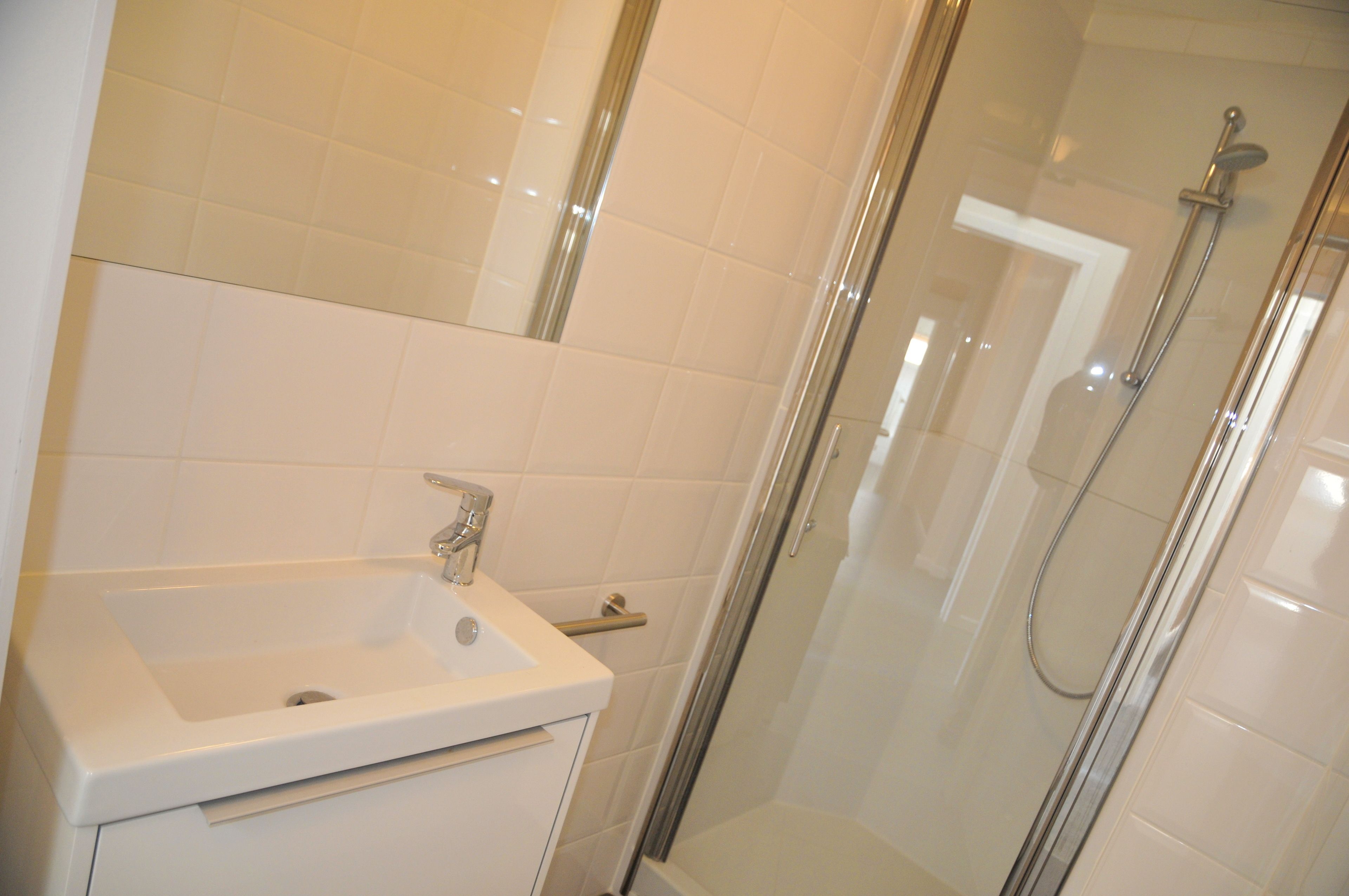 A bathroom with a white sink, a glass shower enclosure, and white tiled walls.