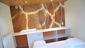 Een slaapkamer met een bed, een witte dressoir, een ingebouwd wastafelmeubel en een muur met giraffeprint.