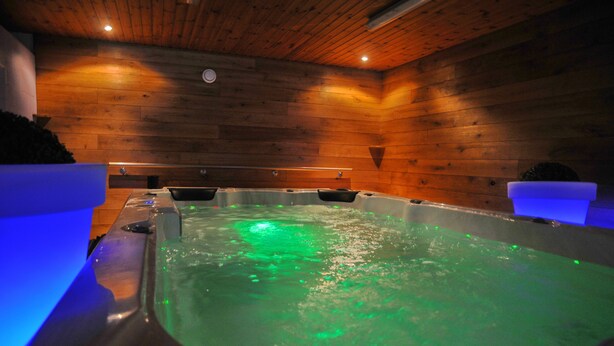 Een hottub met groene verlichting in een houten ruimte.