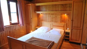 Un dormitorio de cabaña de madera con una cama, mesitas de noche y estanterías empotradas.