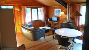 Un interior de cabaña acogedor con sofá, mesa de comedor, sillas, televisor y chimenea.