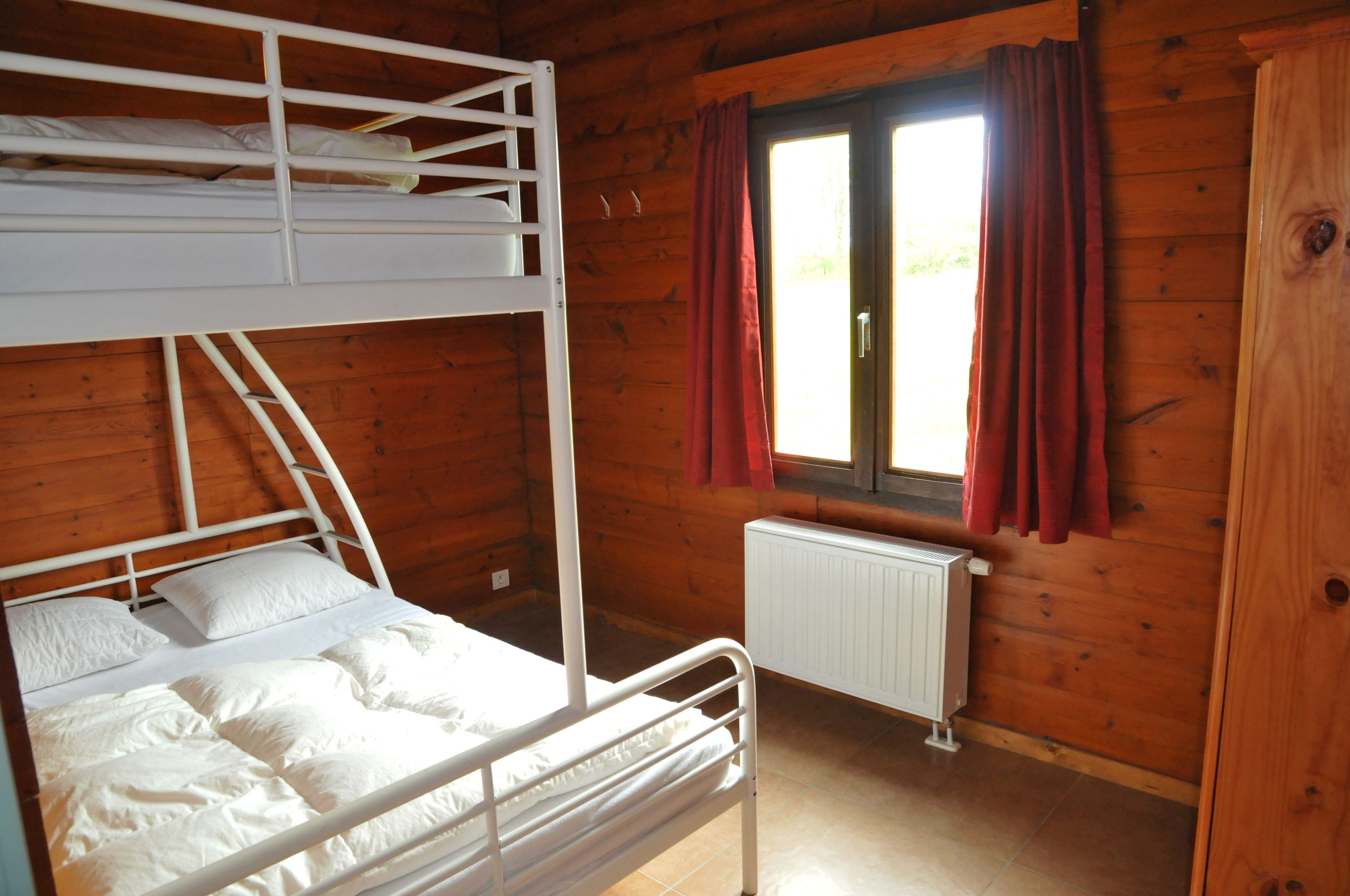 Habitación con literas, ventana, paredes de madera y radiador.