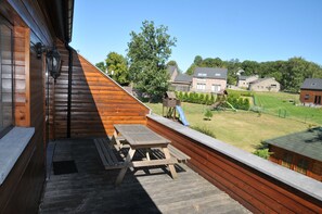A wooden deck with picnic tables and a view of a residential area with houses and a playground. - Vivaldi (Durbuy)