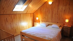 A wooden-paneled room with a bed, two bedside tables with lamps, a skylight, and a wooden crib.