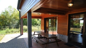 A covered patio area with a wooden picnic table and a glass door leading to an outdoor space.