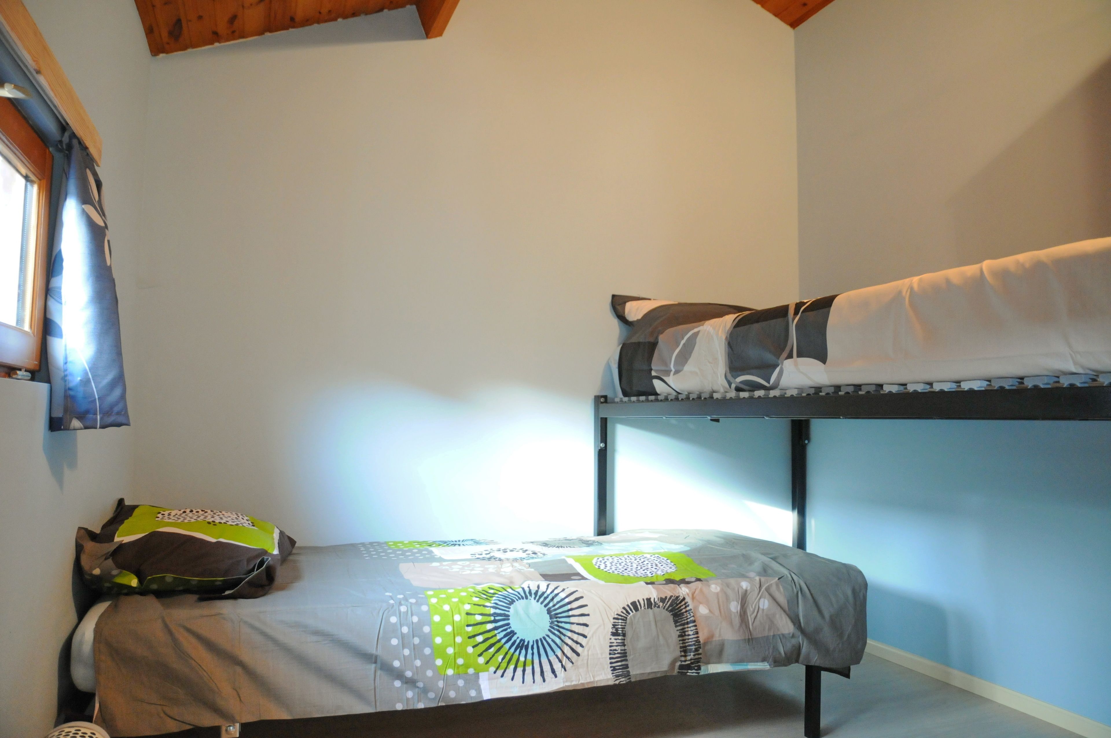 Quarto com beliche, janela, edredom estampado e travesseiro no chão.