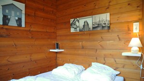 A wooden-paneled room with a bed, a wall-mounted shelf, and a wall-mounted lamp. - Wapiti (Houyet)