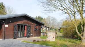 A rustic wooden building with a brick chimney, a covered entrance, and a paved driveway. - Wapiti (Houyet)