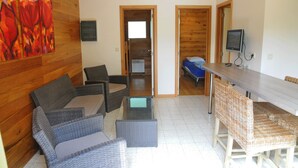 Una habitación con una mesa de comedor, dos sillas de mimbre, una mesa de centro de vidrio y un cuadro en la pared.