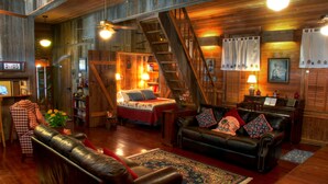 A cozy cabin-style room with a wooden interior, a leather sofa, a bed with a red blanket, a piano, and a staircase.