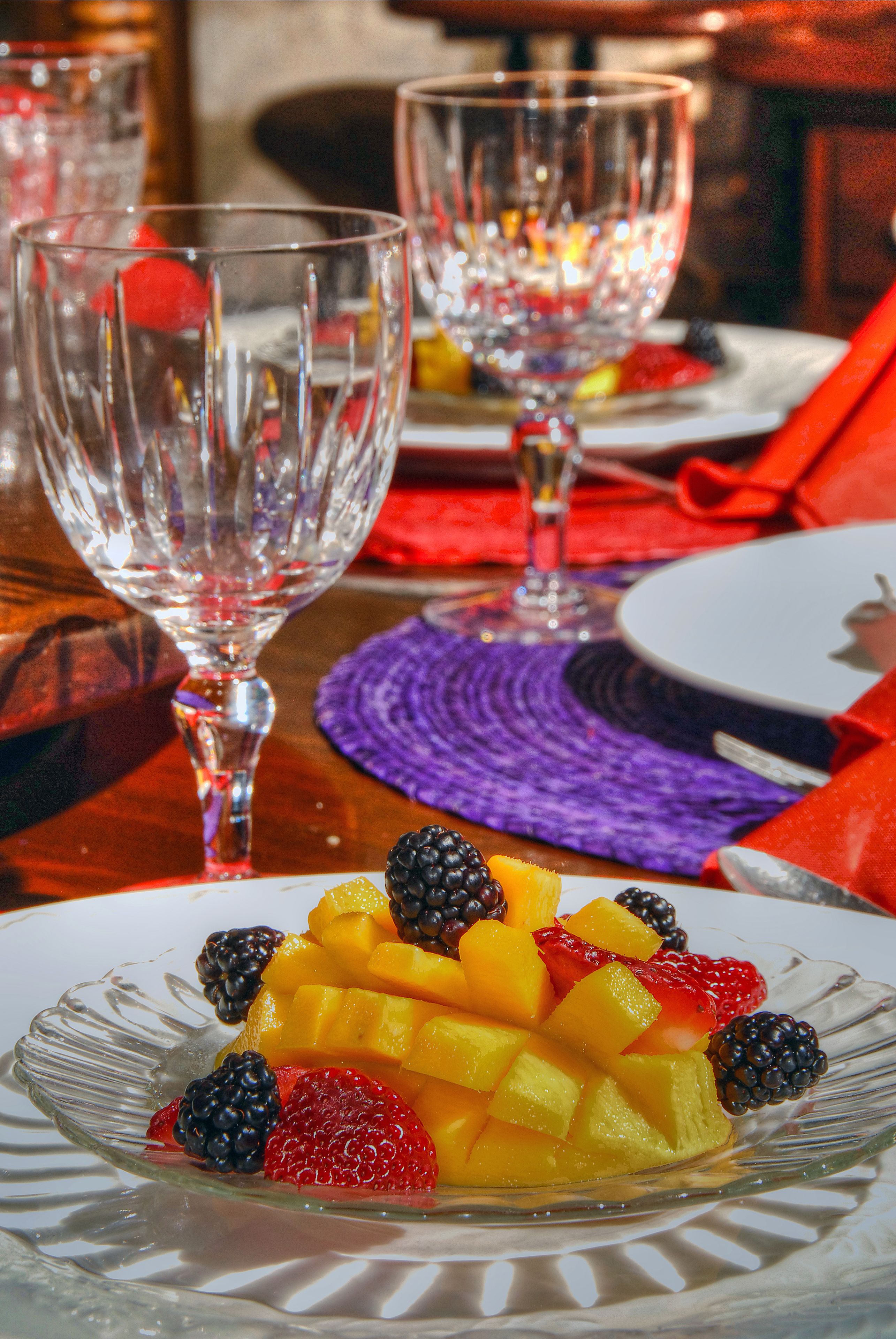 A dining table with a fruit platter, clear glassware, and a purple placemat.