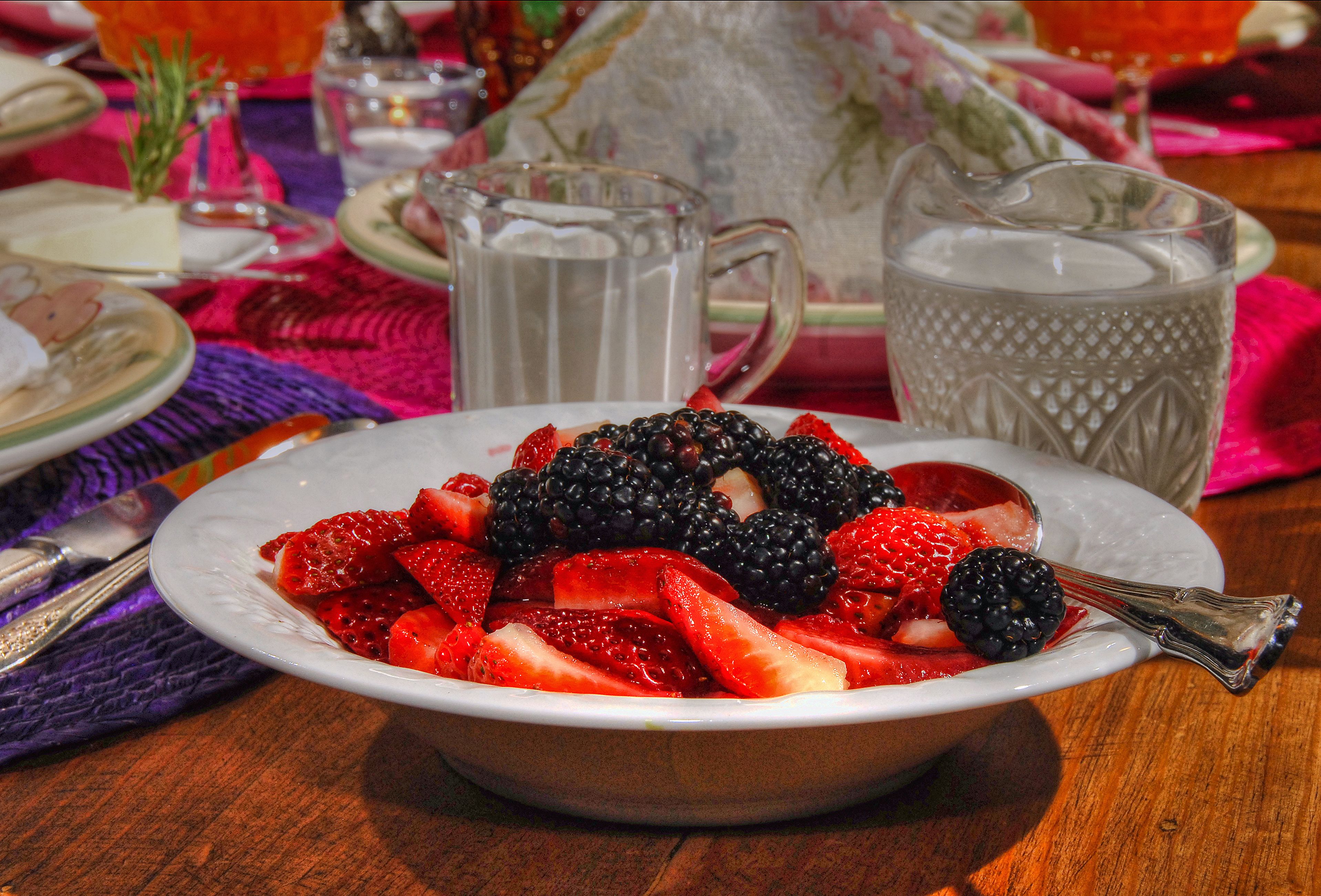 Eine Schüssel mit Beeren und Erdbeeren auf einem Tisch, im Hintergrund eine Karaffe und ein Teekessel.
