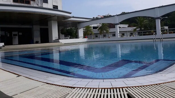 A swimming pool with clear blue water, surrounded by a tiled deck. In the background, there is a multi-story building with balconies and a covered walkway. - SUNSET View Studio Apartment (Langkawi)